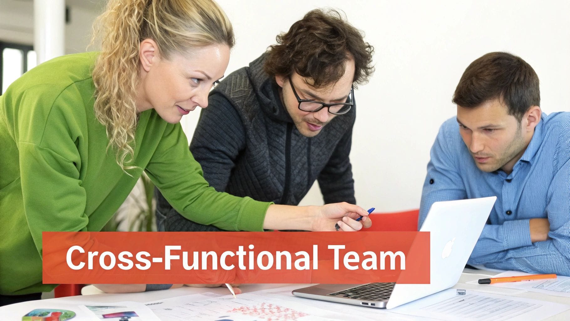 Three people, a cross-functional team, collaboratively working on documents and a laptop at a table.